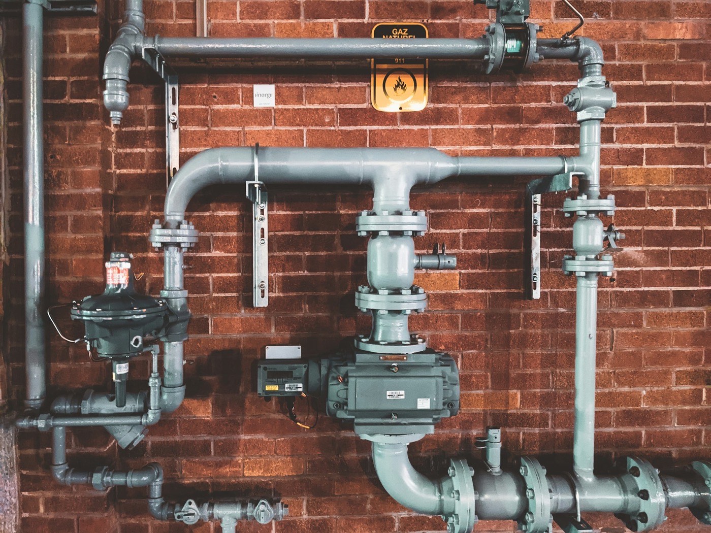 Gas regulator and valve assembly mounted on a brick wall.