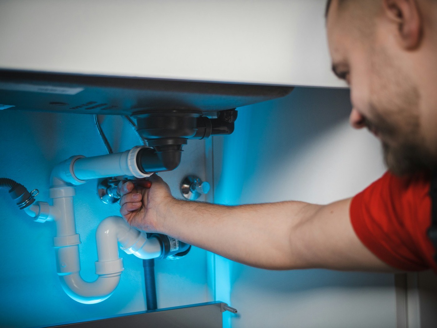Plumber's hands fitting a waste trap under a vanity.